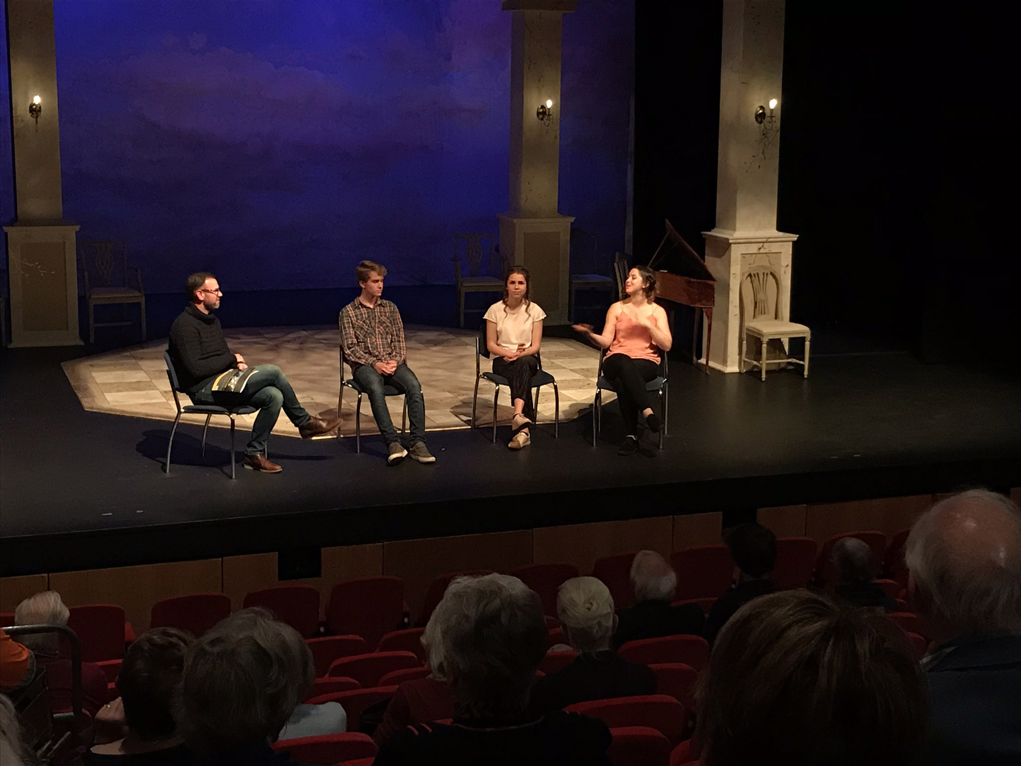 Image shows four people sitting on a stage talking to the audience in a theatre