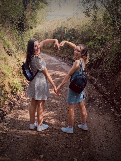 Two girls make a heart shape with their arms in a sunny photo