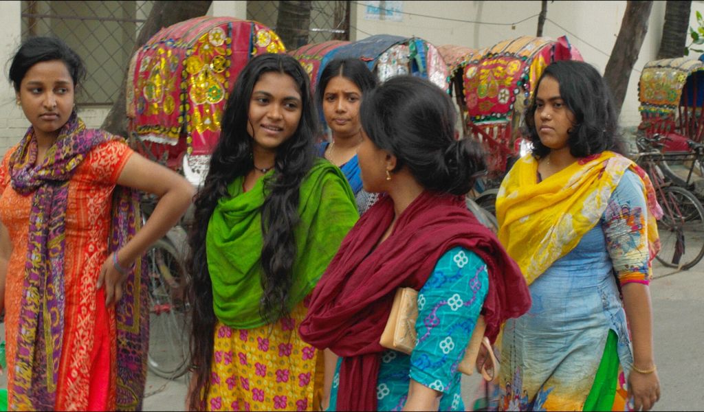 Five Bangladeshi women in brightly coloured Sari's walk down the street chatting in a still from the film Made in Bangladesh