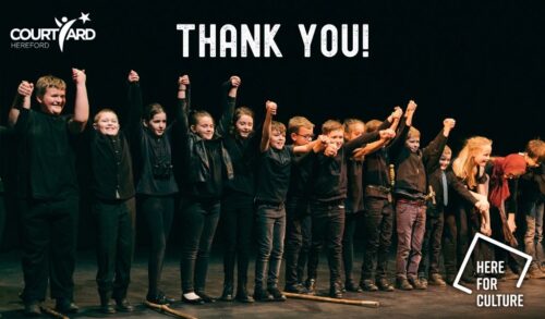 A group of children stand in a line on stage They holding hands raised in the air about to bow The words Thank You are written across the top with the Courtyard Hereford and Here For Culture logos featured