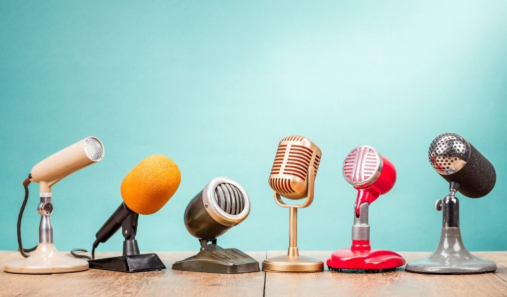 Press - A row of different microphones lined up on a table against a light blue background