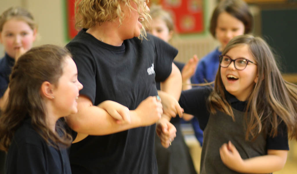 Primary school children linking arms and smiling in a drama workshop