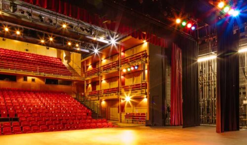 Support Your Theatre imageView from the back of The Courtyards main stage looking out on an empty auditorium the stage lights are shining