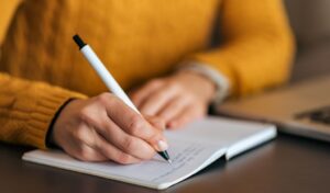 Person wearing a yellow jumper writing on a notepad