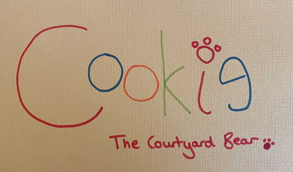 Cookie The Courtyard Bear's signature written in rainbow colours
