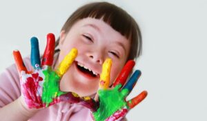 Be A Star Week Online image, a young girl with Down Syndrome holding her paint covered hands up to the camera