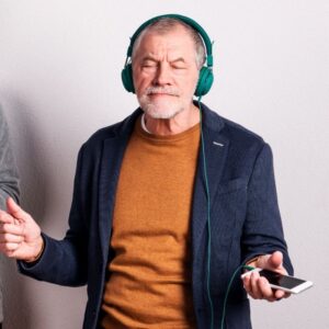 A man with grey hair is listening to music through headphones with his eyes shut