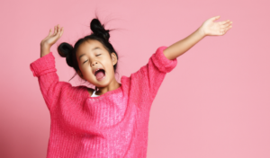 Young girl in a bright pink jumper, singing with her arms in the air