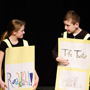 Two young children wearing sandwich boards, one says 'Roald Dahl' the other says 'The Twits'