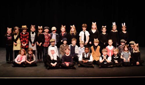 A large group of children in Roald Dahl character costumes stood and sat on The Courtyard stage