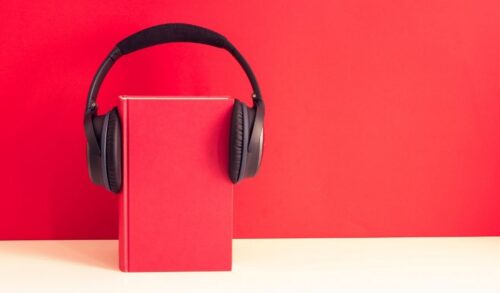 Writing Room Member Produces Radioplay  A red book with headphones on stands against a red background