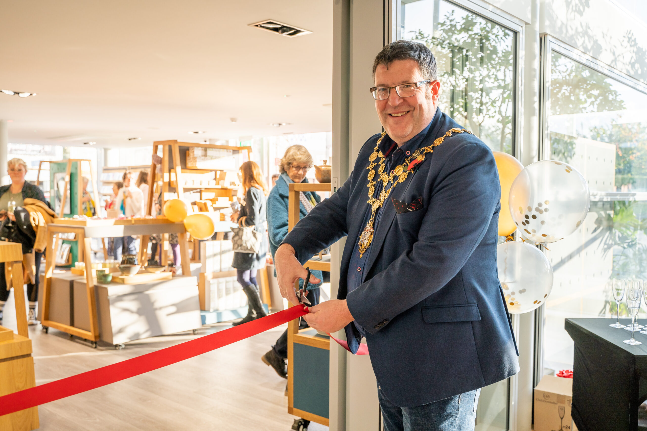 The Right Worshipful the Mayor of Hereford, Councillor Paul Stevens cutting a red ribbon in front of the shop doorway, smiling at the camera