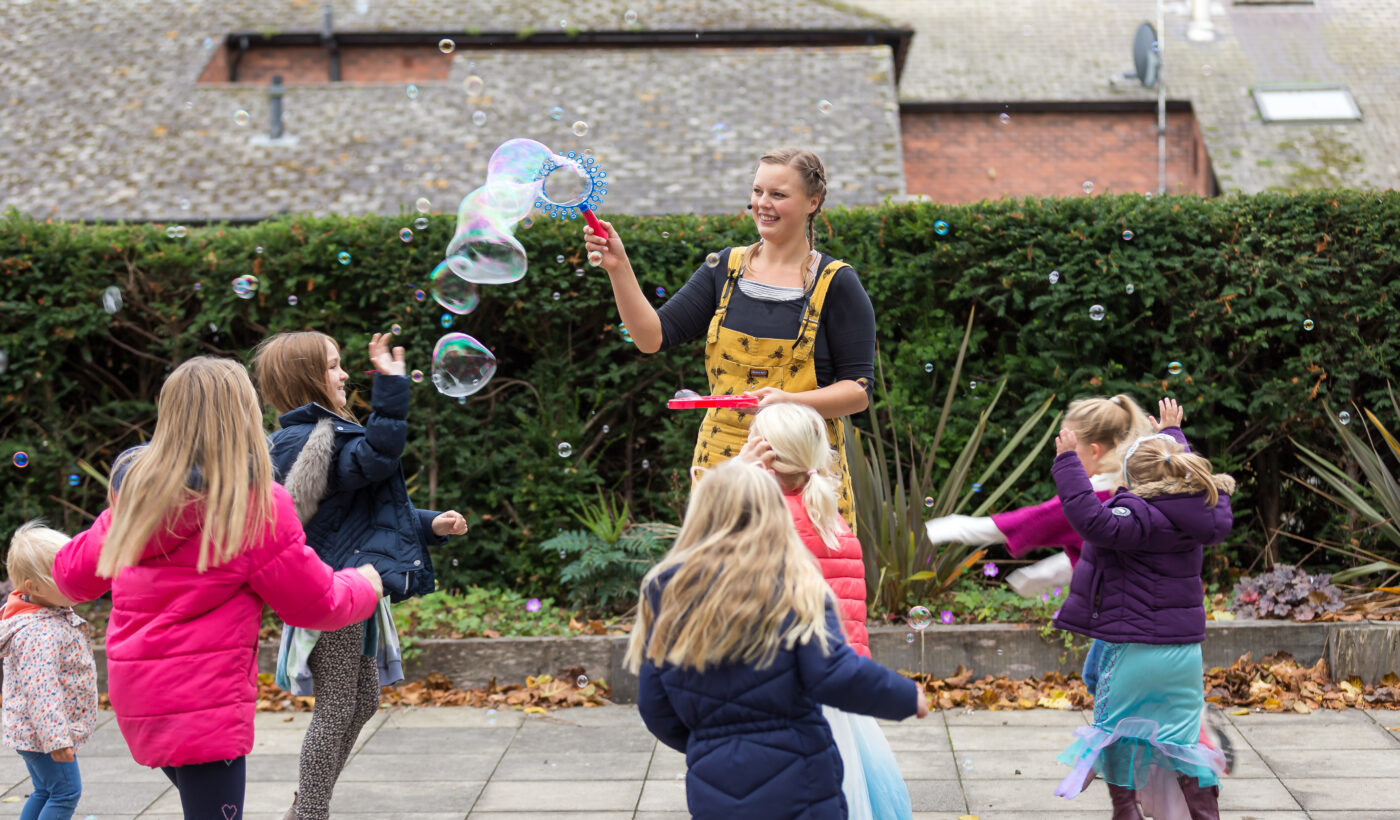 Family Festival: Bee-ology - a woman outside making bubbles in front of a group pf children laughing and dancing