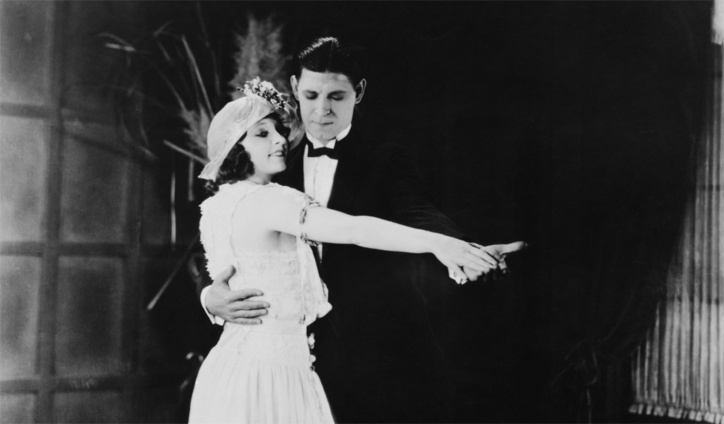 Black and white photo of a woman in a white dress dancing with a man in a suit