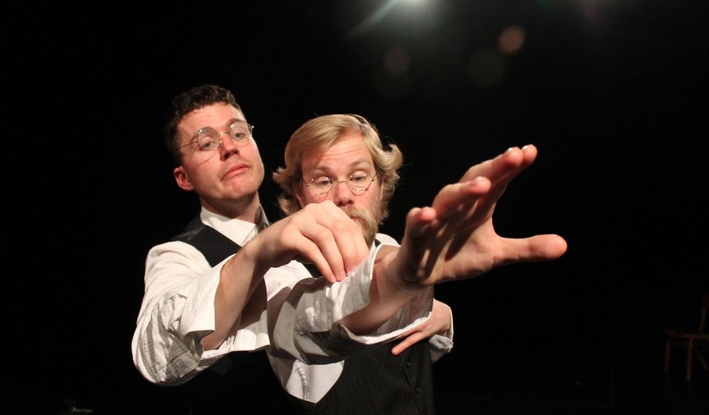 The Endling, image: two men in waistcoats reaching forwards looking quizzically at something on one man's sleeve