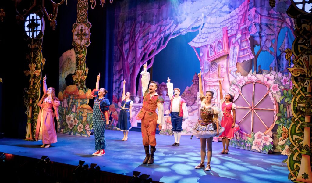 The Courtyard's giant family pantomime receives five-star reviews : the cast onstage smiling with one arm in the air