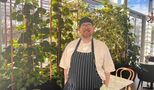 An image of Dickie in chef whites standing in the Chase Lounge smiling at the camera