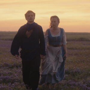 A man and woman walking through a field hand in hand at sunset