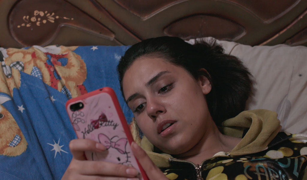 A girl in bed looking concerned at her phone that is in a Hello Kitty case