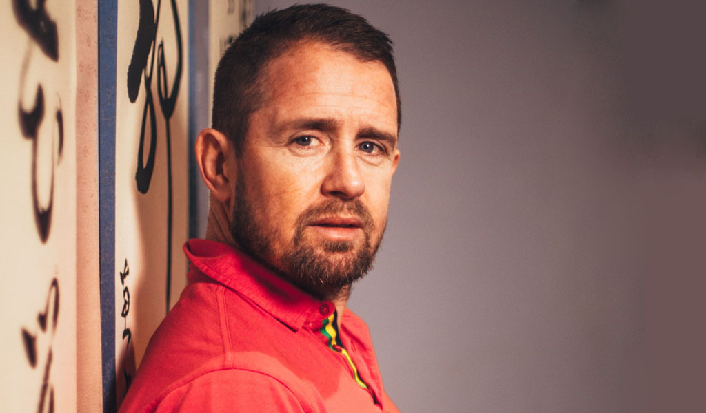 A close up shot of Shane Williams in an orange polo shirt looking at the camera