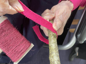 Hands holding a wooden stick and wrapping pink material around it