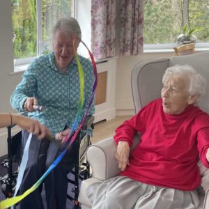 Two older ladies sitting in armchairs, playing with coloured ribbons