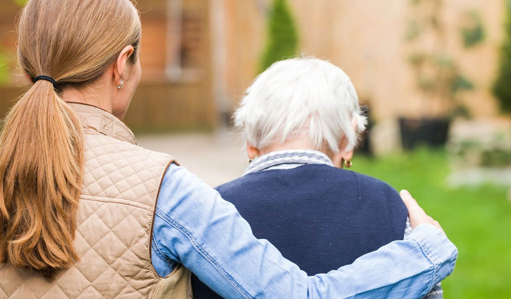 The back of a female carer with her arm around an elderly person
