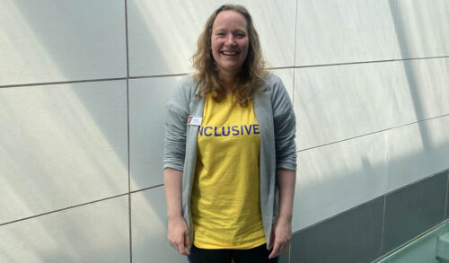 Education Officer and Youth Theatre Leader Kate Ross stood wearing a yellow tshirt and grey cardigan smiling at the camera