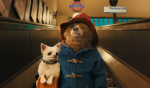 Animated image of Paddington bear going down an escalator in a London underground station, holding a small dog under his arm
