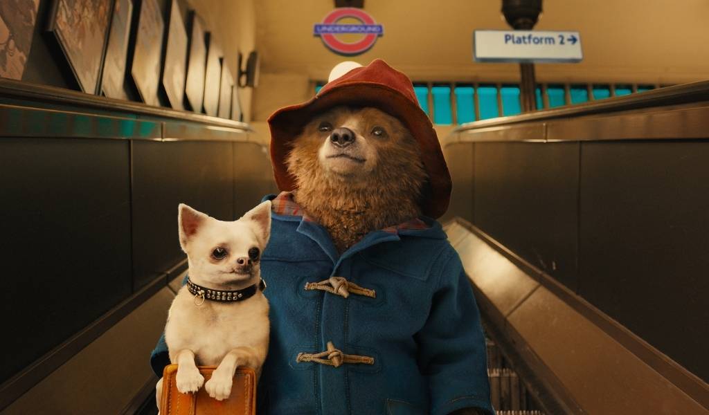 Paddington, Image - Paddington Bear holds a small dog whilst going down an escalator