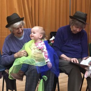 An older lady wearing a hat sitting on a chair with a baby on her lap