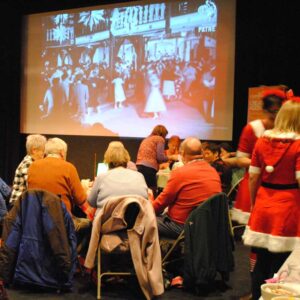 A group of participants at a Christmas Spectacular Tea Dance sitting at tables, drinking tea and watching a black and white film