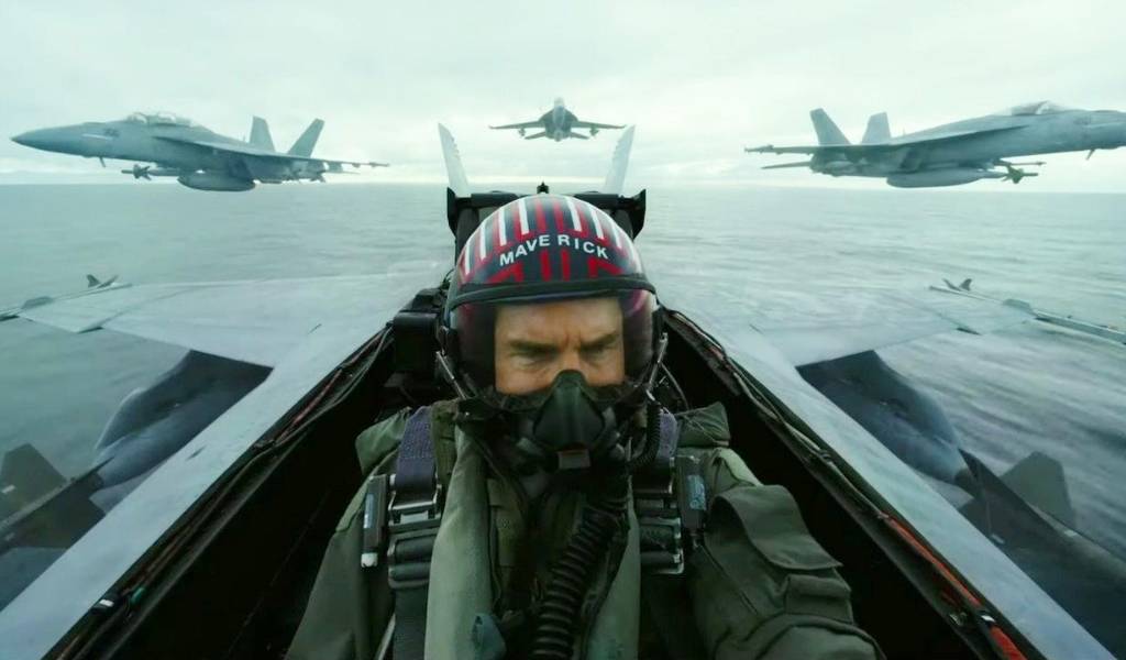 Top Gun: Maverick Image - Tom Cruise sits in the cock pit of a fighter jet as other jets fly behind him