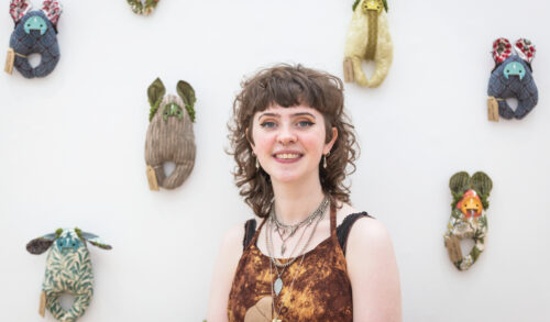 Image  Cultivate artist Lola McCormack stands in in front of her art