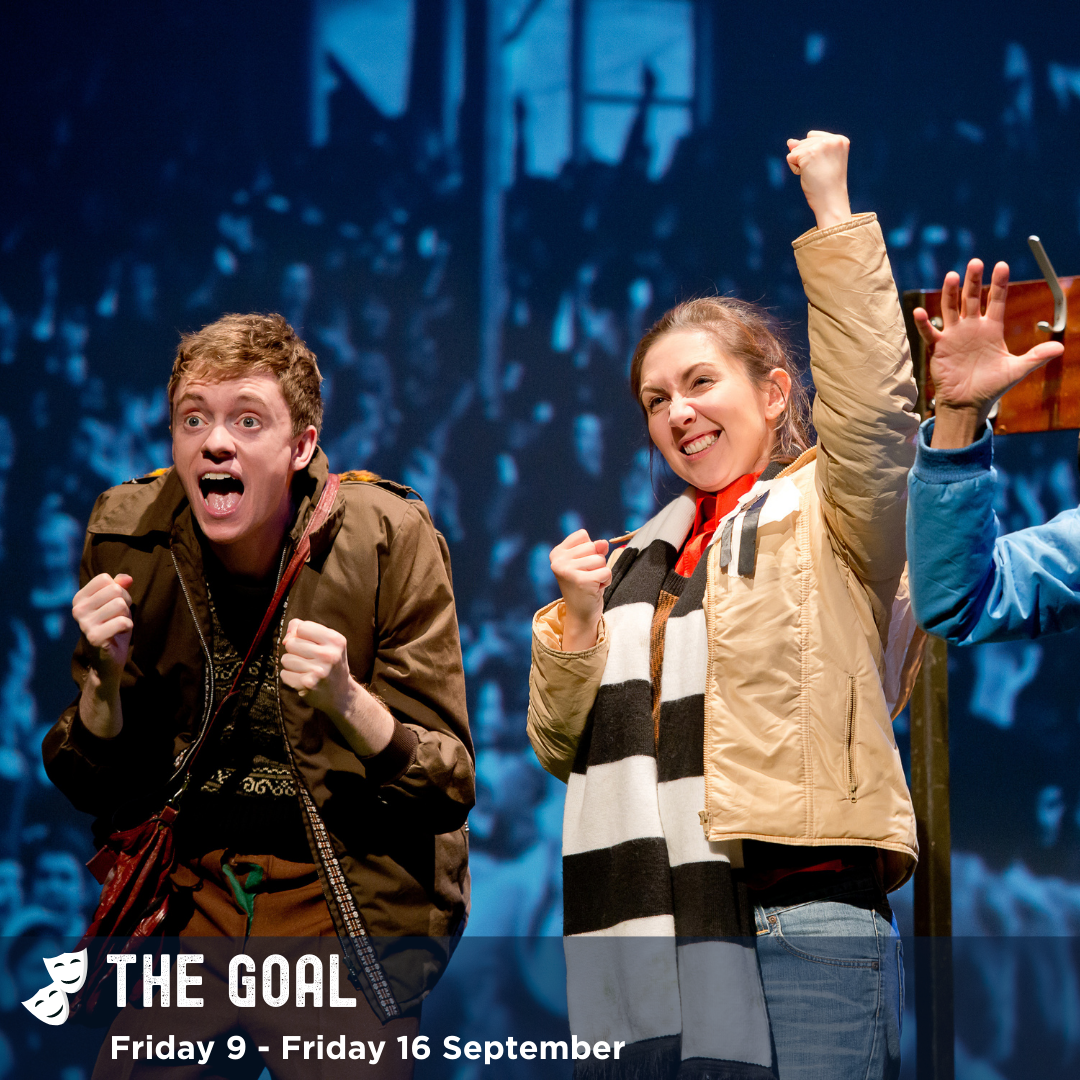 The Goal, image: two actors dressed in coats and scarves, cheering and punching the air