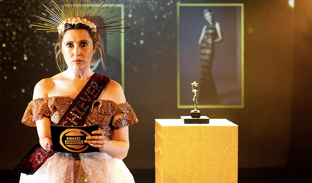 Disabled artist, Melissa Johns in a scrown and a sash, stood next to an award. 