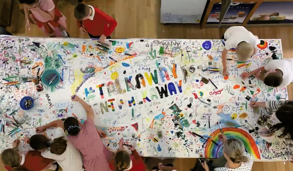 Talk Away, image: a group pf school children standing around a table drawing on a piece of paper that says '#TalkAway'