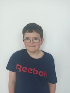 A young boy in a black t-shirt and glasses smiling at the camera
