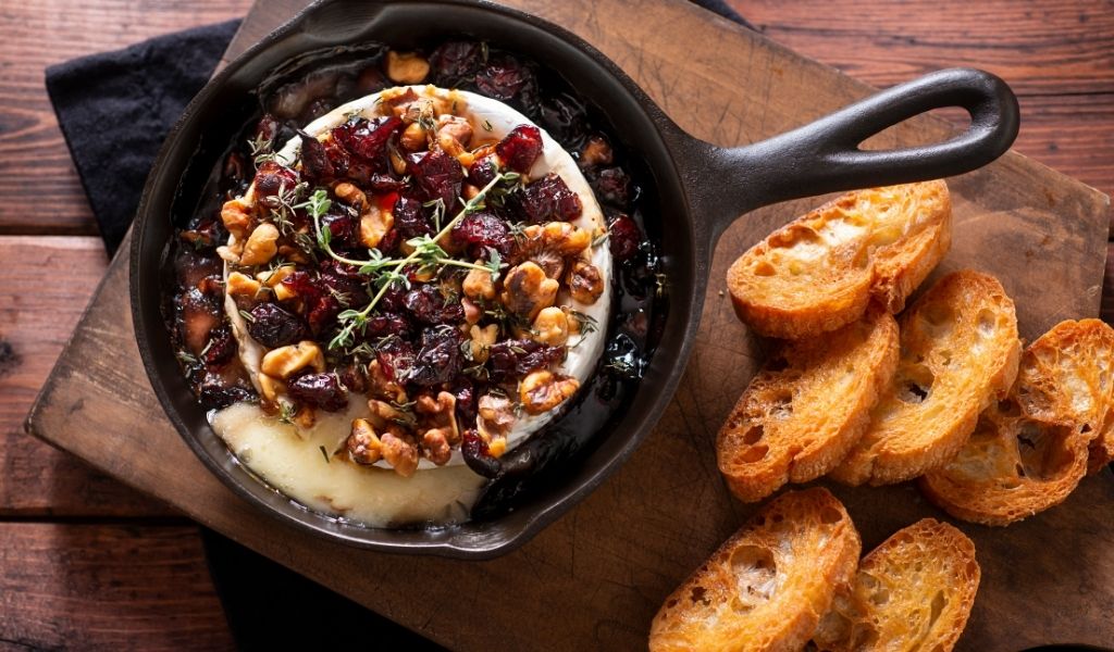 Baked camembert covered in cranberries next to a selection of bruschetta