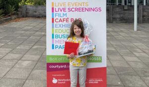 Kid Lit Winner Ophelia Morgan Dew standing in front of The Courtyard building holding her prizes