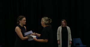 Two women looking at each other smiling and holding hands with another woman stood behind them smiling