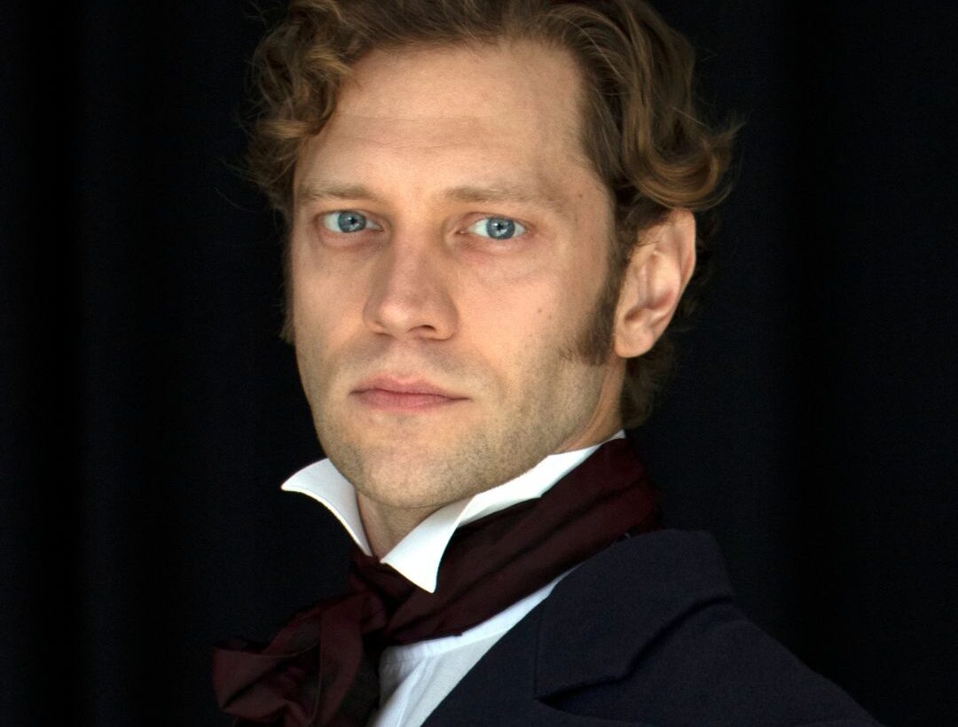 A man wearing Victorian dress looking intently straight at the camera
