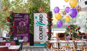 Panto launch - a pull up banner for Beauty and the Beast and a pull up banner for The Courtyard surrounded by roses and purple and gold balloons