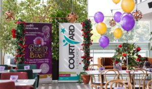 Panto launch - a pull up banner for Beauty and the Beast and a pull up banner for The Courtyard surrounded by roses and purple and gold balloons