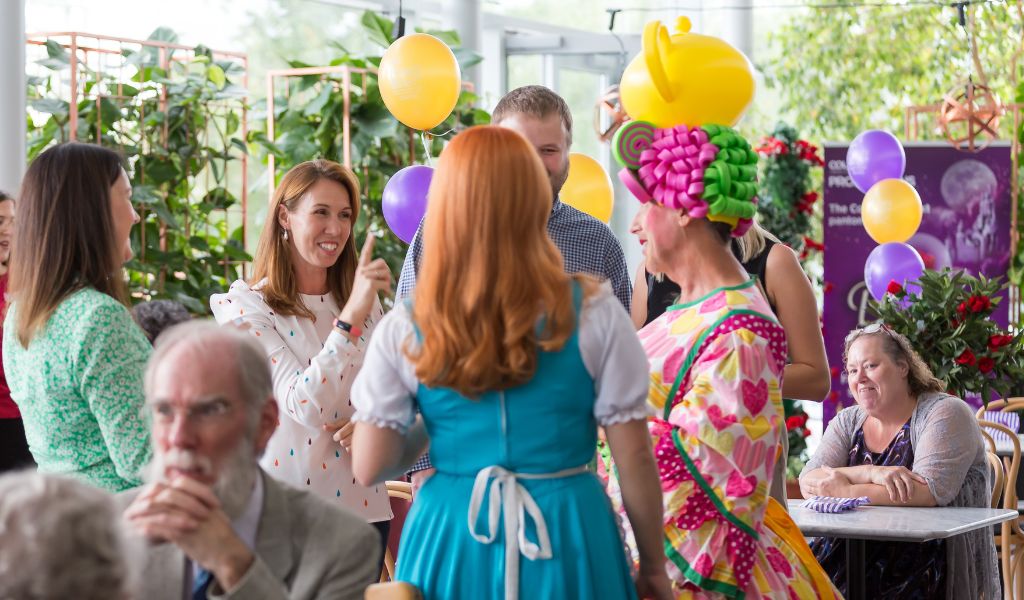 A group of people includin g members of The Courtyard Board stand talking to members of the panto cast in costume