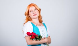 A woman wearing a blue and white dress holding a bunch of roses and looking off thoughtfully into the distance