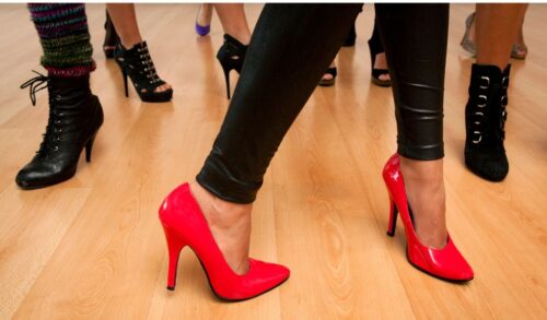 A pair of feet on a dance floor wearing bright red heels