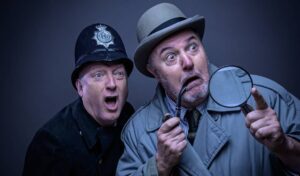 A man dressed as a policeman stands next to a man dressed as an inspector holding a spy glass. Both looked shocked.