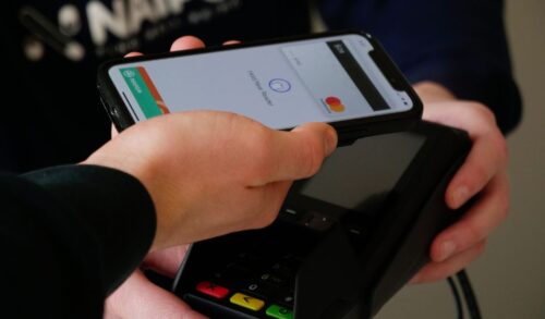 A hand holding a phone making a payment on a card machine