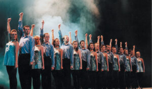 A row of dancers standing with one arm in the air
